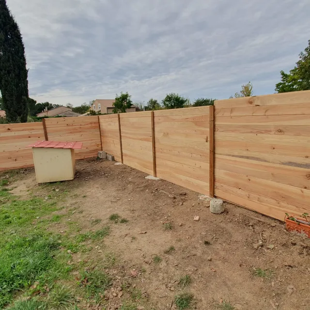 Clôture en bois en cours de pose sur un terrain en terre